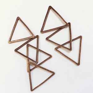 May include: Six copper triangle shaped metal charms. The charms are all the same size and shape, and they are arranged in a random pattern.