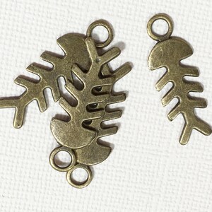 May include: Three antique gold-toned metal charms in the shape of fish bones. The charms have a loop at the top for attaching to jewelry or other crafts.