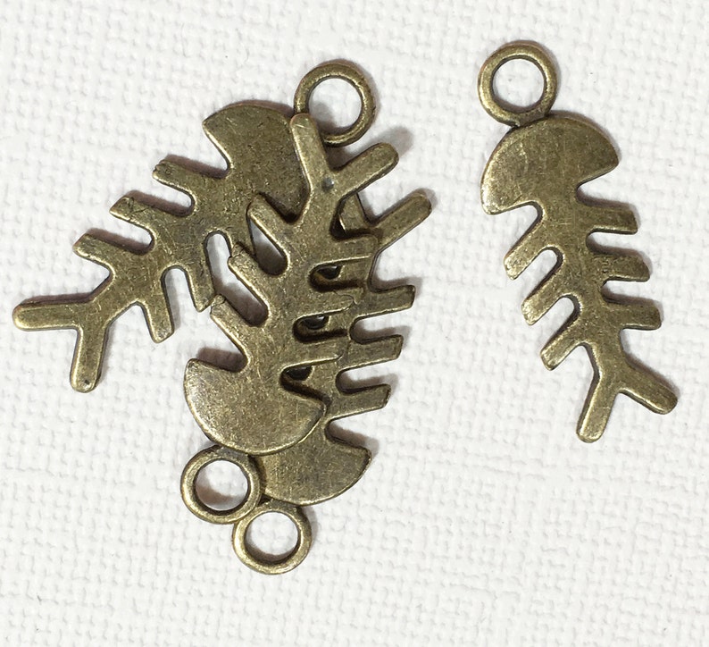 May include: Three antique gold-toned metal charms in the shape of fish bones. The charms have a loop at the top for attaching to jewelry or other crafts.