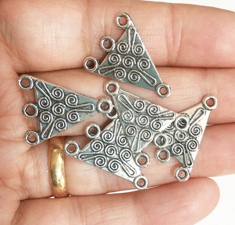 May include: Five silver triangle-shaped metal connector charms with a swirl design. Each charm has three holes for attaching jewelry.