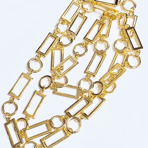 May include: A gold chain necklace featuring rectangular links and circular connectors. The chain is crafted from metal and has a polished finish.