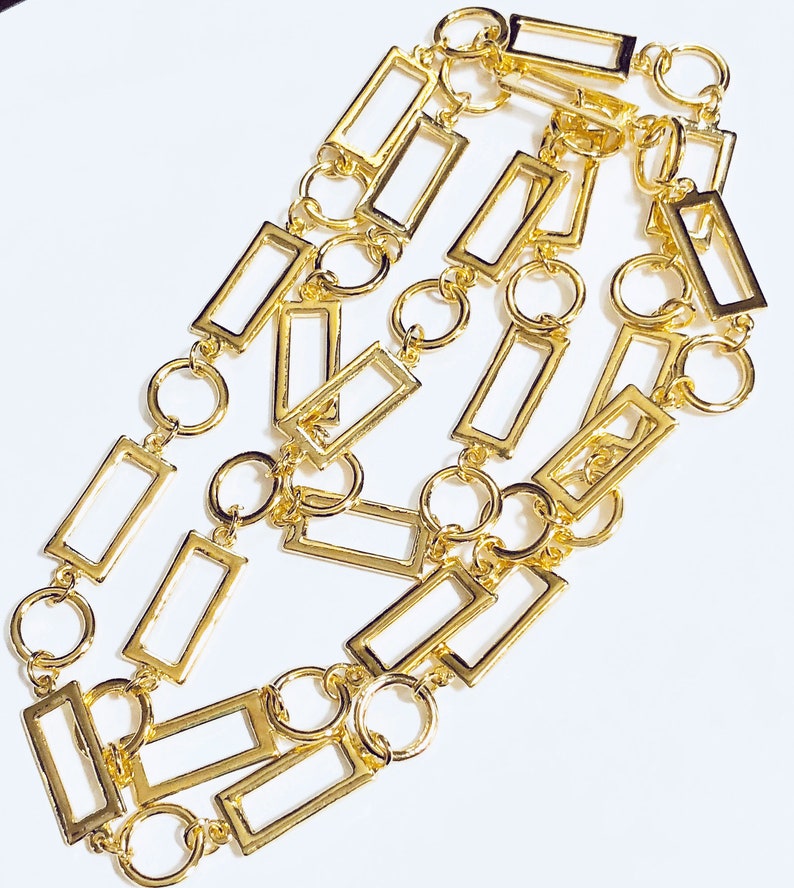 May include: A gold chain necklace featuring rectangular links and circular connectors. The chain is crafted from metal and has a polished finish.