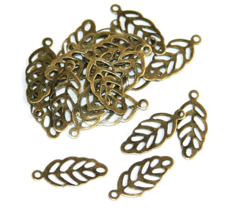 May include: A collection of antique bronze-colored metal leaf charms, each featuring a delicate filigree cutout design with a small circular loop at the top for attachment. These small, lightweight jewelry components are arranged in a cluster.
