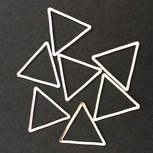 Puede incluir: Siete dijes de metal de forma triangular de color plateado. Los dijes son todos del mismo tamaño y forma, y están dispuestos en un patrón aleatorio.