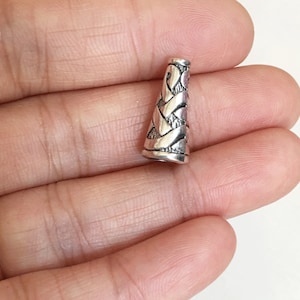 May include: Silver metal cone bead with a braided design.
