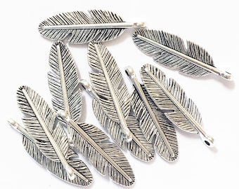 Op de afbeelding: Een groep van tien zilverkleurige metalen verencharms met een gestructureerd oppervlak. Elke charme heeft een lus aan de bovenkant om te bevestigen aan sieraden of andere knutselwerkjes.