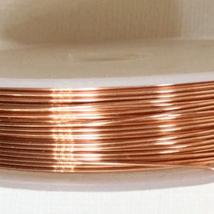 Può includere: Un rotolo di filo di rame, avvolto strettamente su un rotolo di plastica bianco. Il filo è di un colore marrone rossiccio caldo.