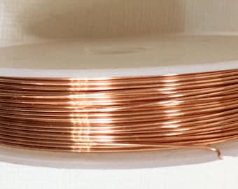 May include: A spool of copper wire, wound tightly on a white plastic spool. The wire is a warm, reddish-brown color.