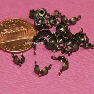 May include: A pile of antique brass-colored metal bead caps with a loop on each side. The bead caps are about the size of a US penny.