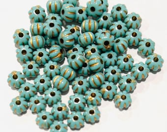 May include: A large pile of turquoise blue glass beads with gold accents. The beads are round and have a raised, flower-like design.
