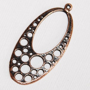 May include: A copper-colored oval pendant with a textured surface and a pattern of small circles cut out. The pendant has a loop at the top for hanging.