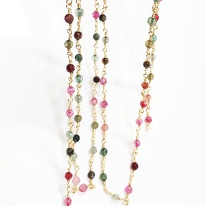 May include: A gold chain necklace with multi-colored beads. The beads are a mix of pink, green, and brown.