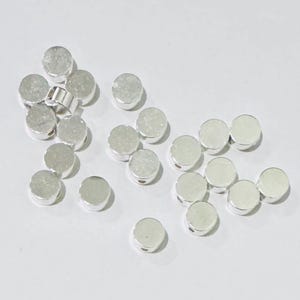 Op de afbeelding: Een verzameling zilverkleurige ronde kralen met een getextureerd oppervlak. De kralen hebben een gat in het midden om te rijgen.