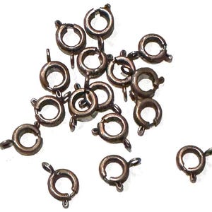 May include: A group of 18 gold-toned metal jump rings, each with a spring-loaded clasp. The rings are scattered on a white background.