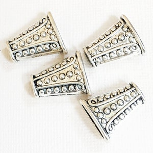 May include: Four silver metal cone-shaped bead caps with a beaded and textured design.