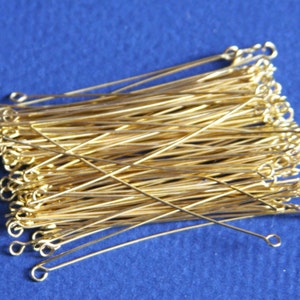 May include: A pile of gold-colored head pins with a loop at one end. The pins are arranged in a criss-cross pattern.
