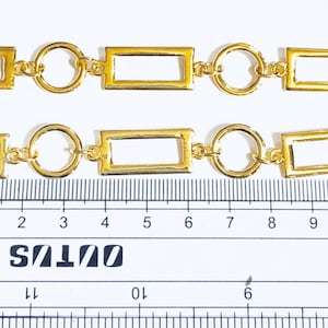 May include: Gold chain with rectangular and round links. The chain is measured against a ruler, showing it is approximately 10 centimetres long.