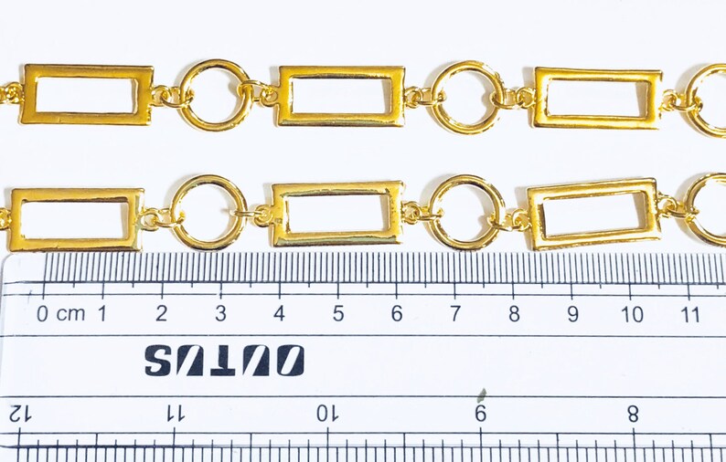 May include: Gold chain with rectangular and round links. The chain is measured against a ruler, showing it is approximately 10 centimetres long.