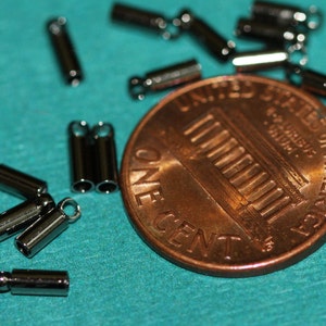 Puede incluir: Primer plano de una moneda de un centavo de d&oacute;lar estadounidense con un mont&oacute;n de tapas de extremo de metal plateadas, tambi&eacute;n conocidas como cuentas de crimpado, esparcidas a su alrededor. Las tapas de extremo se utilizan para la fabricaci&oacute;n de joyas.