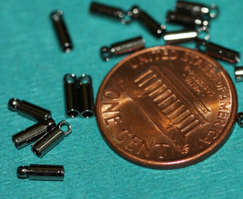 Puede incluir: Primer plano de una moneda de un centavo de d&oacute;lar estadounidense con un mont&oacute;n de tapas de extremo de metal plateadas, tambi&eacute;n conocidas como cuentas de crimpado, esparcidas a su alrededor. Las tapas de extremo se utilizan para la fabricaci&oacute;n de joyas.