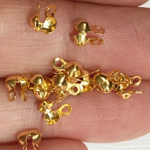May include: A close-up of a pile of gold-toned metal crimp beads with a loop on each side. The beads are small and round, and they are perfect for adding a touch of elegance to jewelry projects.