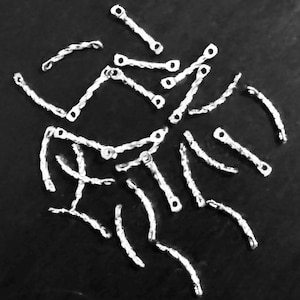 Puede incluir: Una colección de anillas de salto de metal plateadas, cada una con un diseño retorcido. Las anillas están dispersas sobre una superficie negra.