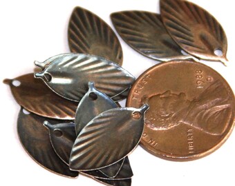 May include: A collection of small, antique bronze-colored metal leaf charms with embossed vein details and a single hole at the top for attachment, displayed next to a 1988 United States copper penny for a clear visual size reference.