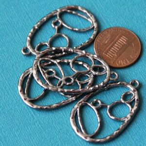 May include: Four silver oval-shaped metal charms with a decorative, intricate design of circles and ovals. The charms are about the size of a US penny.