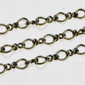 Puede incluir: Primer plano de una cadena dorada con un diseño de eslabón ovalado retorcido. La cadena está hecha de metal y tiene un acabado brillante.