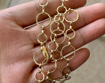 May include: A gold chain necklace with a repeating pattern of interlocking circles. The chain is made of small, round links.