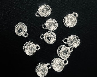 May include: A collection of silver-toned charms with clear rhinestone accents. Each charm features a round rhinestone surrounded by a silver-toned metal frame.