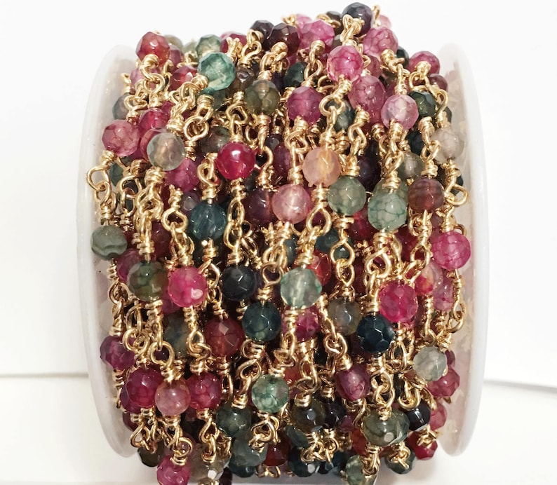 May include: A spool of gold chain with faceted gemstone beads in shades of pink, green, and brown. The beads are strung on a gold chain and are approximately 6mm in diameter.