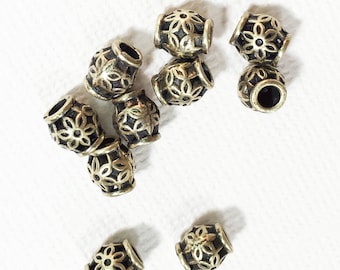 May include: A group of ten silver metal beads with a floral design. The beads are round and have a hole in the center. They are scattered on a white surface.