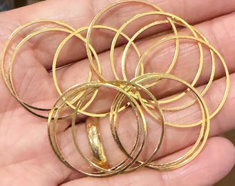 May include: A set of 10 gold-colored metal hoops, each with a slightly different diameter, are stacked and arranged in a circular pattern. The hoops are smooth and shiny, and they appear to be made of a thin metal.