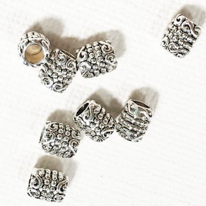 Pode incluir: Um conjunto de dez contas de metal prateadas com um padr&atilde;o de espiral decorativo. As contas medem aproximadamente 2,5 cm de comprimento e t&ecirc;m um acabamento liso e polido.