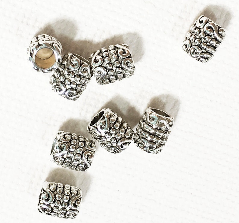 Pode incluir: Um conjunto de dez contas de metal prateadas com um padr&atilde;o de espiral decorativo. As contas medem aproximadamente 2,5 cm de comprimento e t&ecirc;m um acabamento liso e polido.