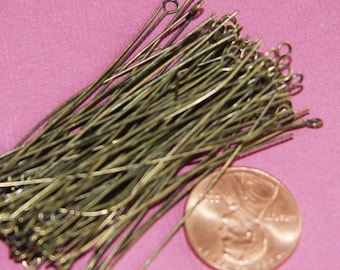 May include: A pile of gold-colored metal headpins with a loop at one end. The headpins are about 1 inch long and are arranged in a random pattern. A US penny is included for scale.
