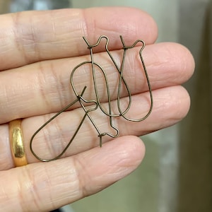 May include: Three gold-toned earring hooks, two are shaped like a U and one is a teardrop shape.