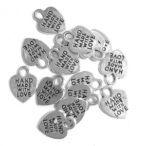 May include: A collection of silver-toned metal heart-shaped charms, each featuring a small loop at the top for attachment. The surface of every charm is embossed with the text "HAND MADE WITH LOVE" in clear, capitalized black lettering.