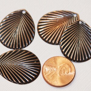 May include: Four copper-colored metal leaf-shaped charms with a ridged design. The charms have a hole at the top for attaching to jewelry or other crafts.