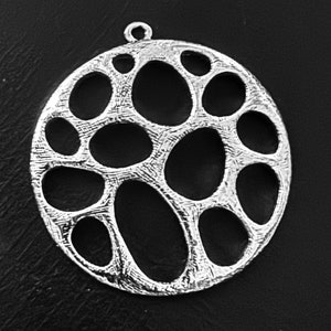 Op de afbeelding: Een zilveren hanger met een rond ontwerp met een patroon van met elkaar verbonden cirkels en ovalen. De hanger heeft een glad, getextureerd oppervlak.
