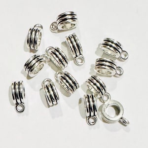 May include: A group of silver-toned metal bead caps with a decorative grooved design. The caps have a small loop at the top for attaching to jewellery.