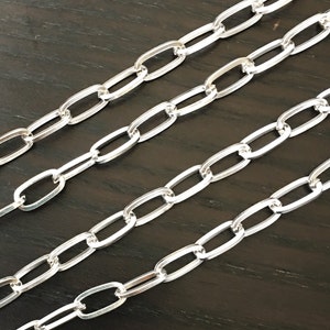 May include: Four strands of silver chain with oval links. The chain is laid out in parallel lines on a dark wood surface.