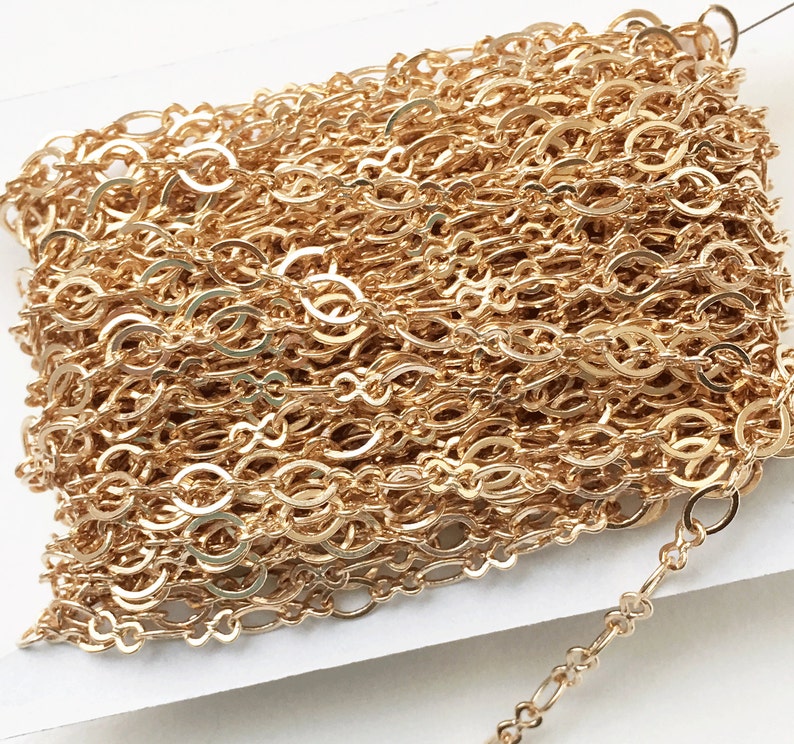 May include: A close-up of a gold chain with a delicate, interwoven design. The chain is made of small, oval-shaped links that are connected together in a repeating pattern.