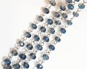 May include: A strand of blue crystal beads strung on a silver chain. The beads are faceted and have a shimmery finish.