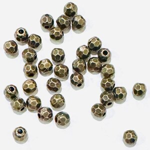 Pu&ograve; includere: Una collezione di 25 perline in metallo color oro antico. Le perline sono rotonde e hanno una superficie sfaccettata e testurizzata.