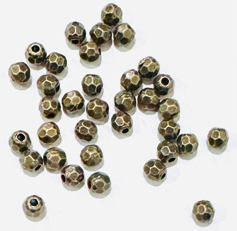 Pu&ograve; includere: Una collezione di 25 perline in metallo color oro antico. Le perline sono rotonde e hanno una superficie sfaccettata e testurizzata.