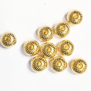 May include: Ten gold-colored metal beads with a textured surface and a hole in the center. The beads are round and have a slightly domed shape.