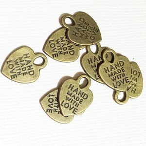 May include: A group of six gold heart-shaped metal tags with the text "HAND MADE WITH LOVE" on each tag. The tags have a hole at the top for attaching to a product.