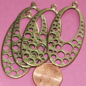 May include: Four antique brass oval-shaped earring blanks with a decorative circle pattern. The blanks have a hole at the top for attaching earring hooks.